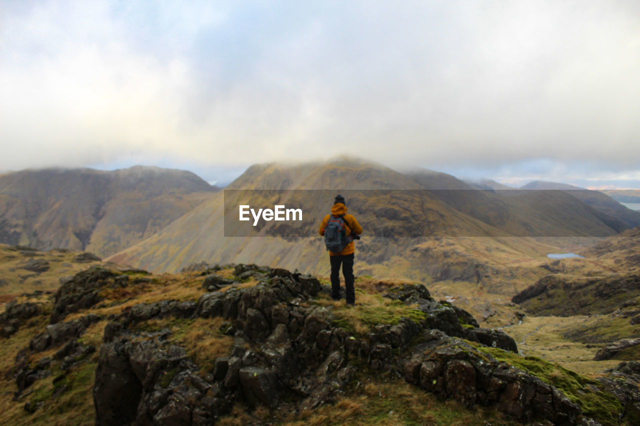 Rear view of man standing on mountain against sky