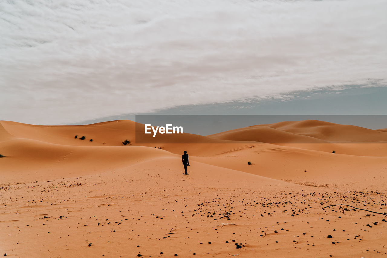 Man on sand dune in desert against sky