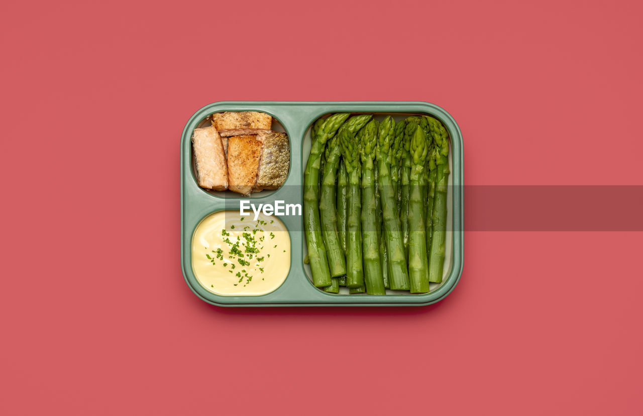 Above view  lunch box prepared with baked asparagus, salmon fish, and hollandaise sauce. meal prep.