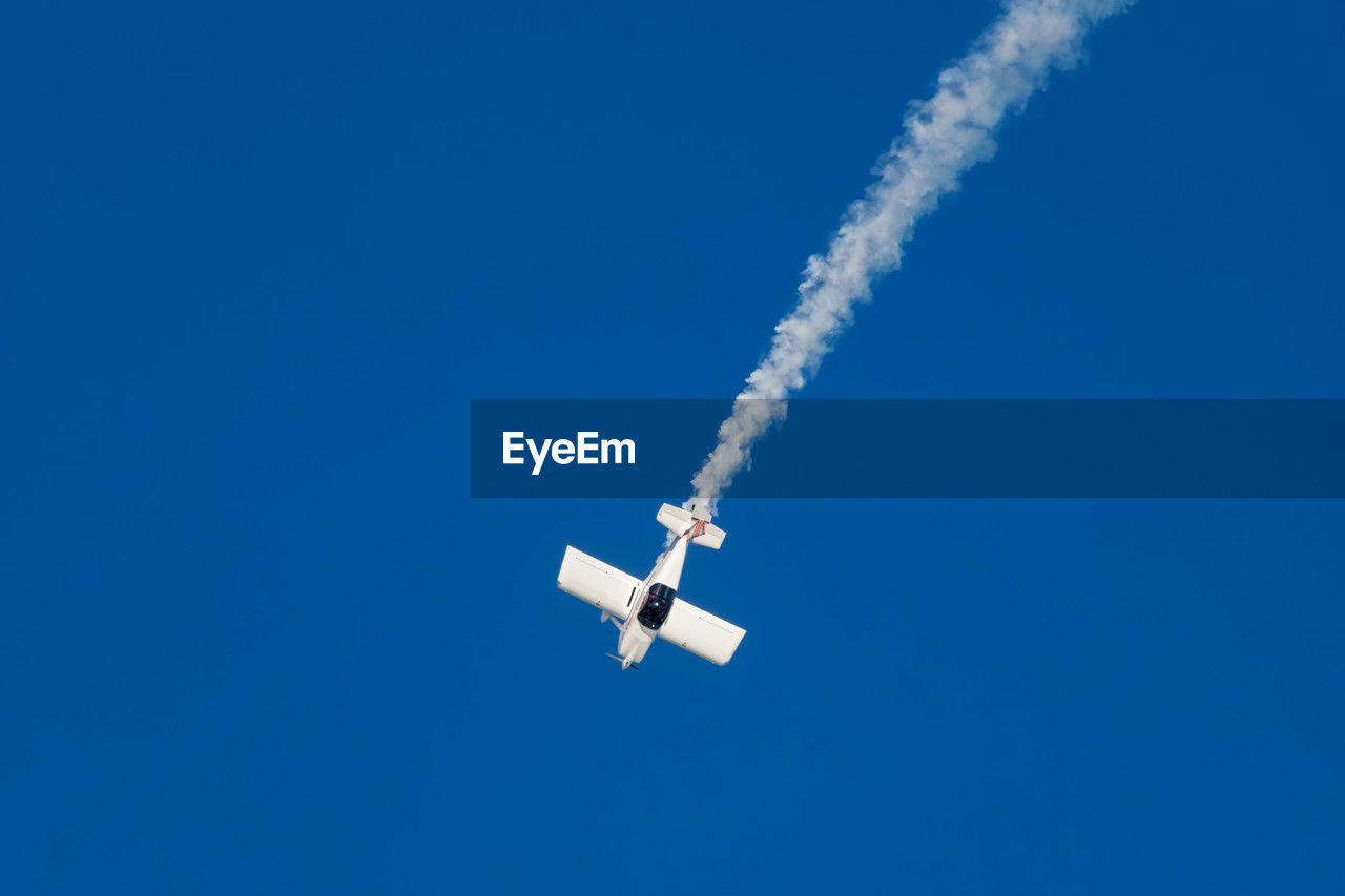 air vehicle, airplane, transportation, vapor trail, flying, sky, mode of transportation, blue, on the move, air show, clear sky, cloud, smoke, no people, nature, vehicle, low angle view, motion, mid-air, day, wing, copy space, outdoors, aircraft, sunny, aerobatics, travel