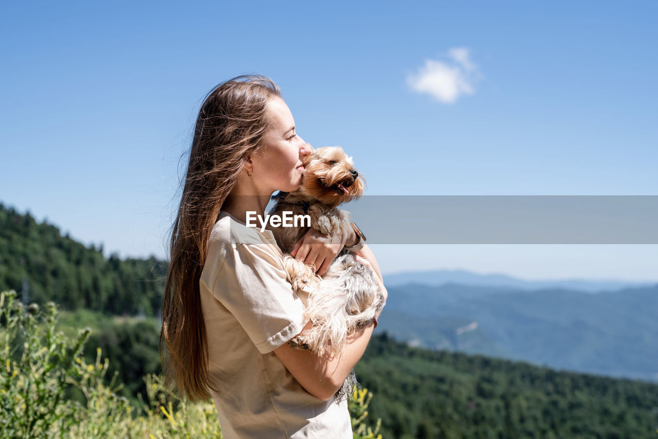 Young woman holding small dog puppy yorkshire terrier hiking at the mountains