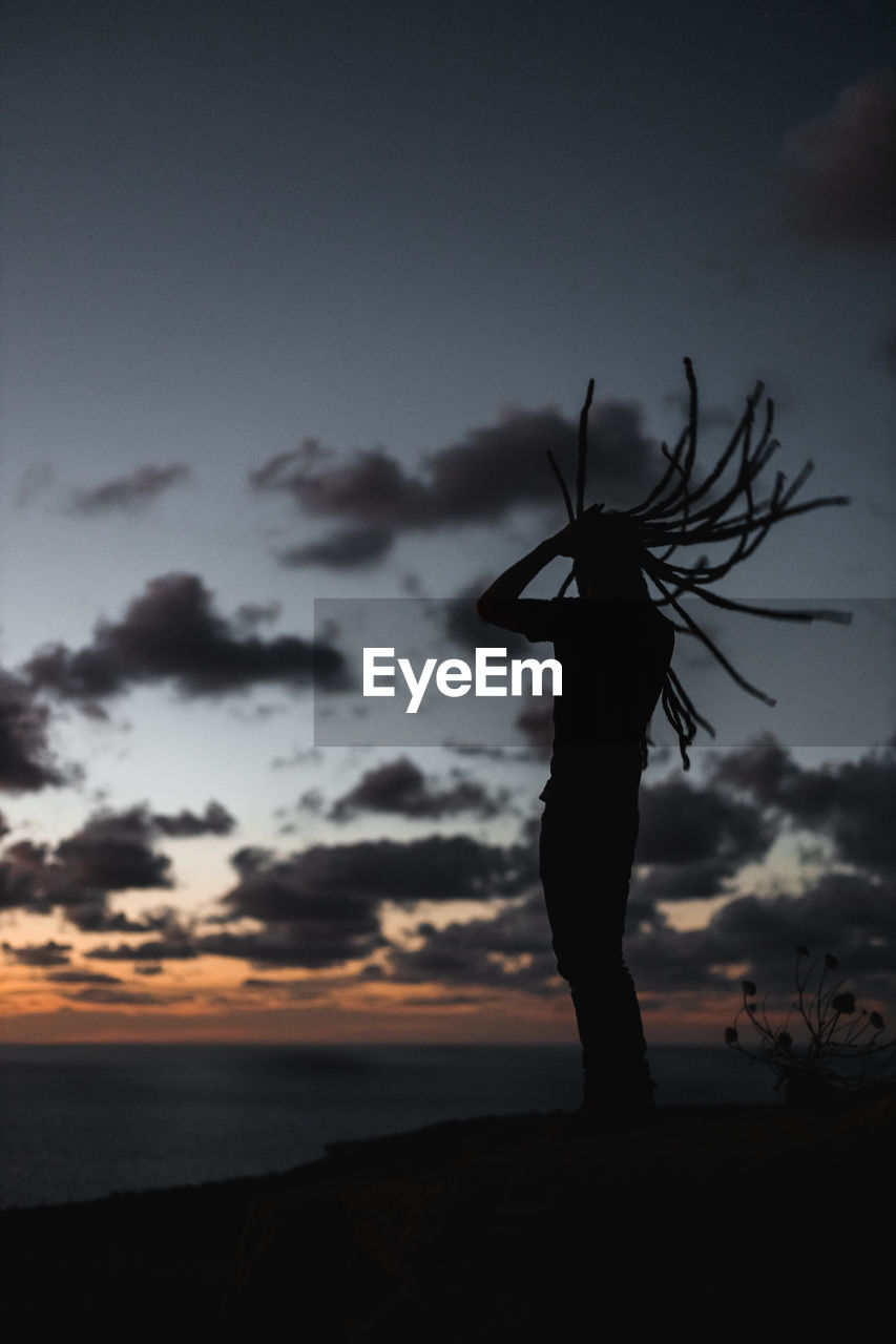 Silhouette person with dreadlocks standing on land against sky during sunset 