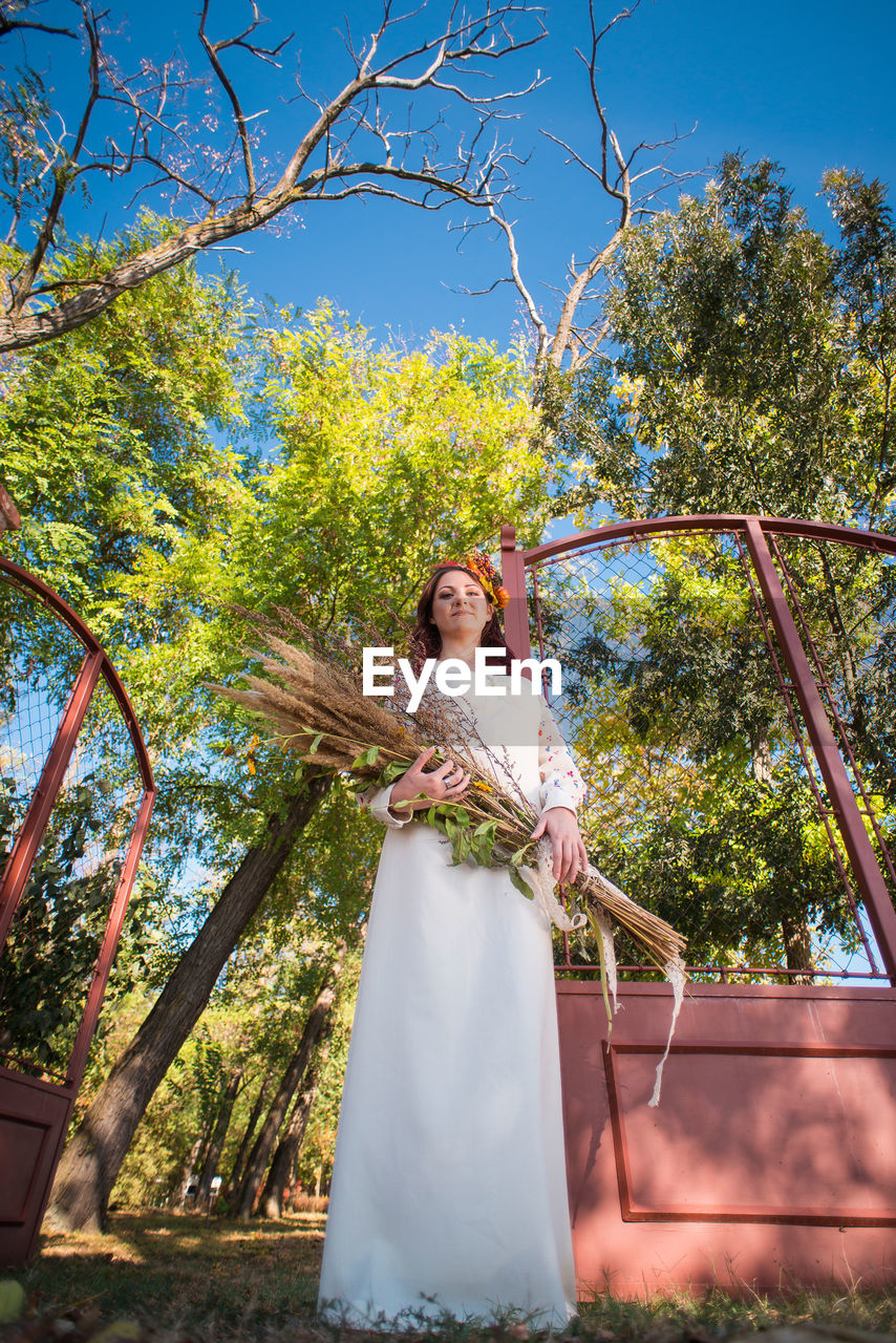 Portrait of young woman holding plants against trees