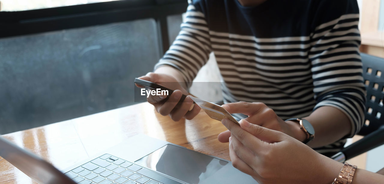 MIDSECTION OF WOMAN USING MOBILE PHONE IN RESTAURANT