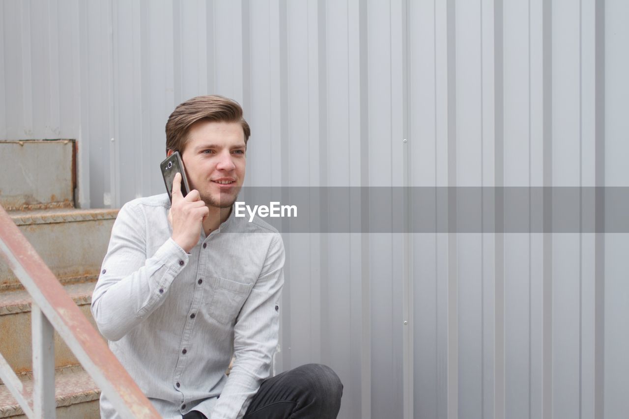 Smiling young man answering mobile phone while sitting on stairs