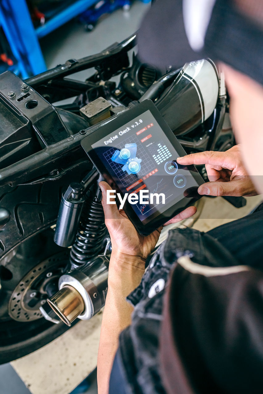 Mature mechanic using digital tablet by motorcycle in garage