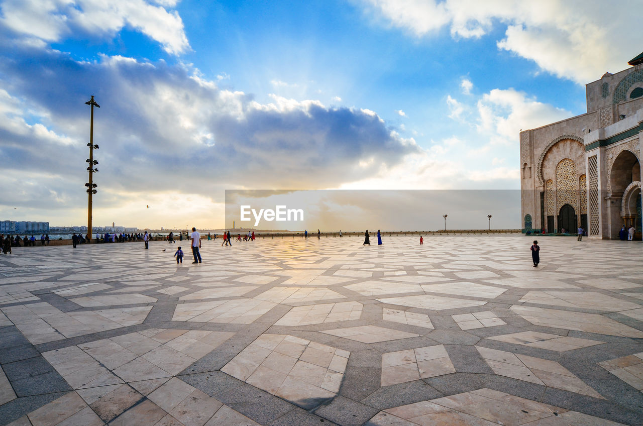 People at mosque hassan ii against sky in city