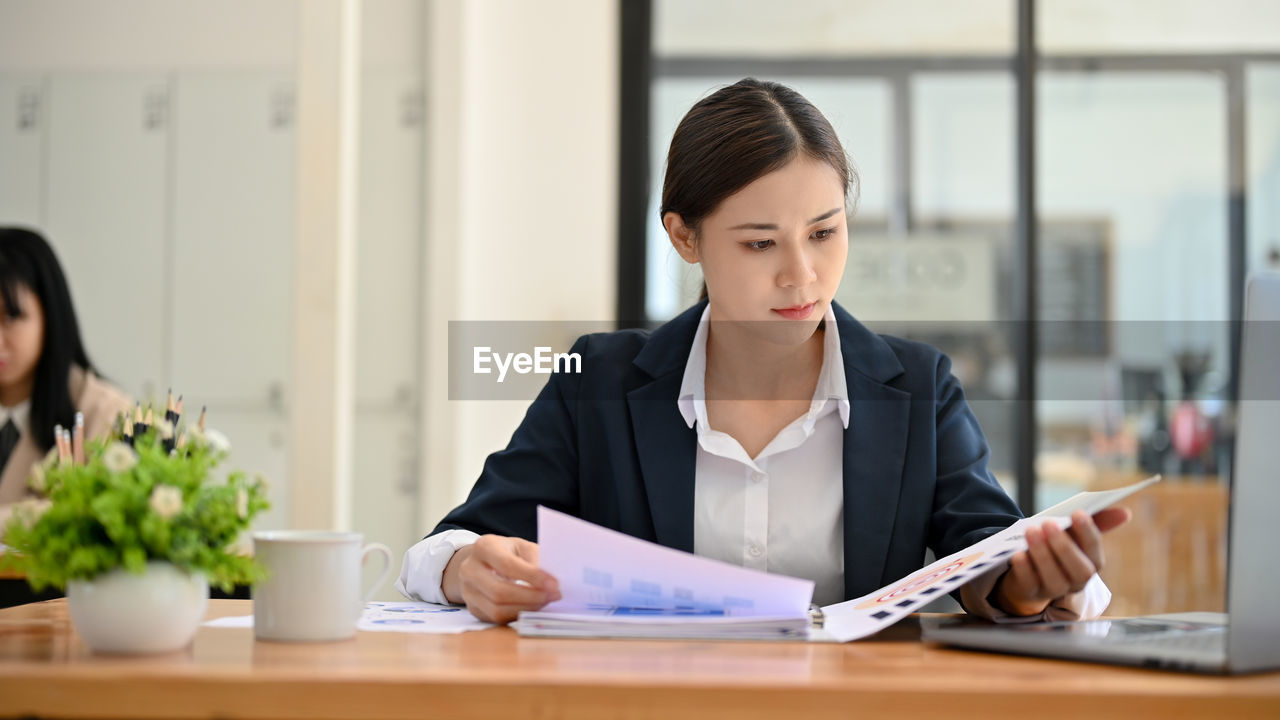 young woman using mobile phone while sitting on table in office