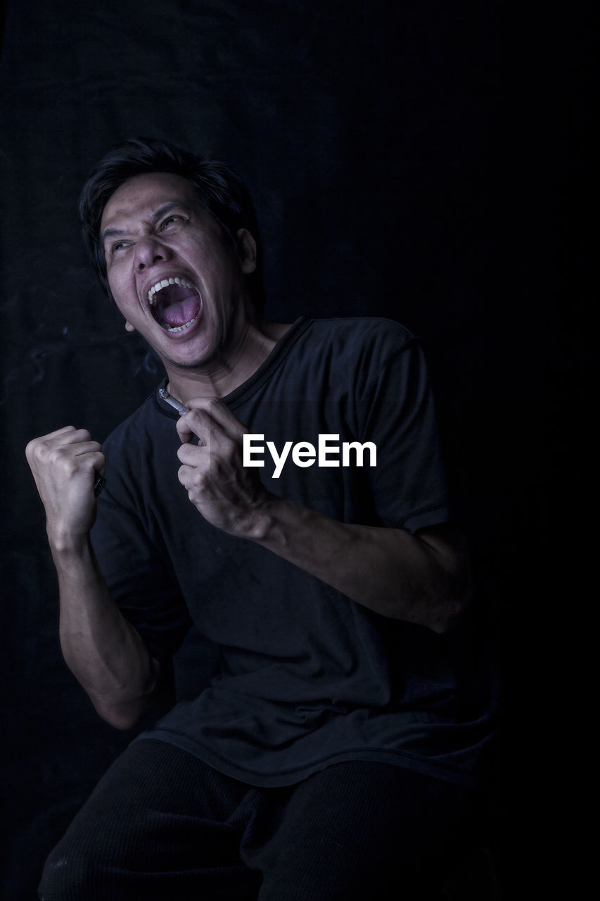 Angry man smoking cigarette against black background