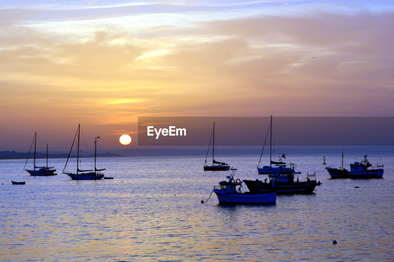 Sailboats in sea against sky during sunset