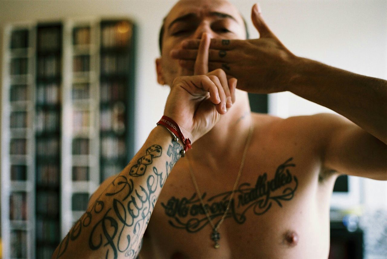 Portrait of tattooed man with hands covering mouth at home