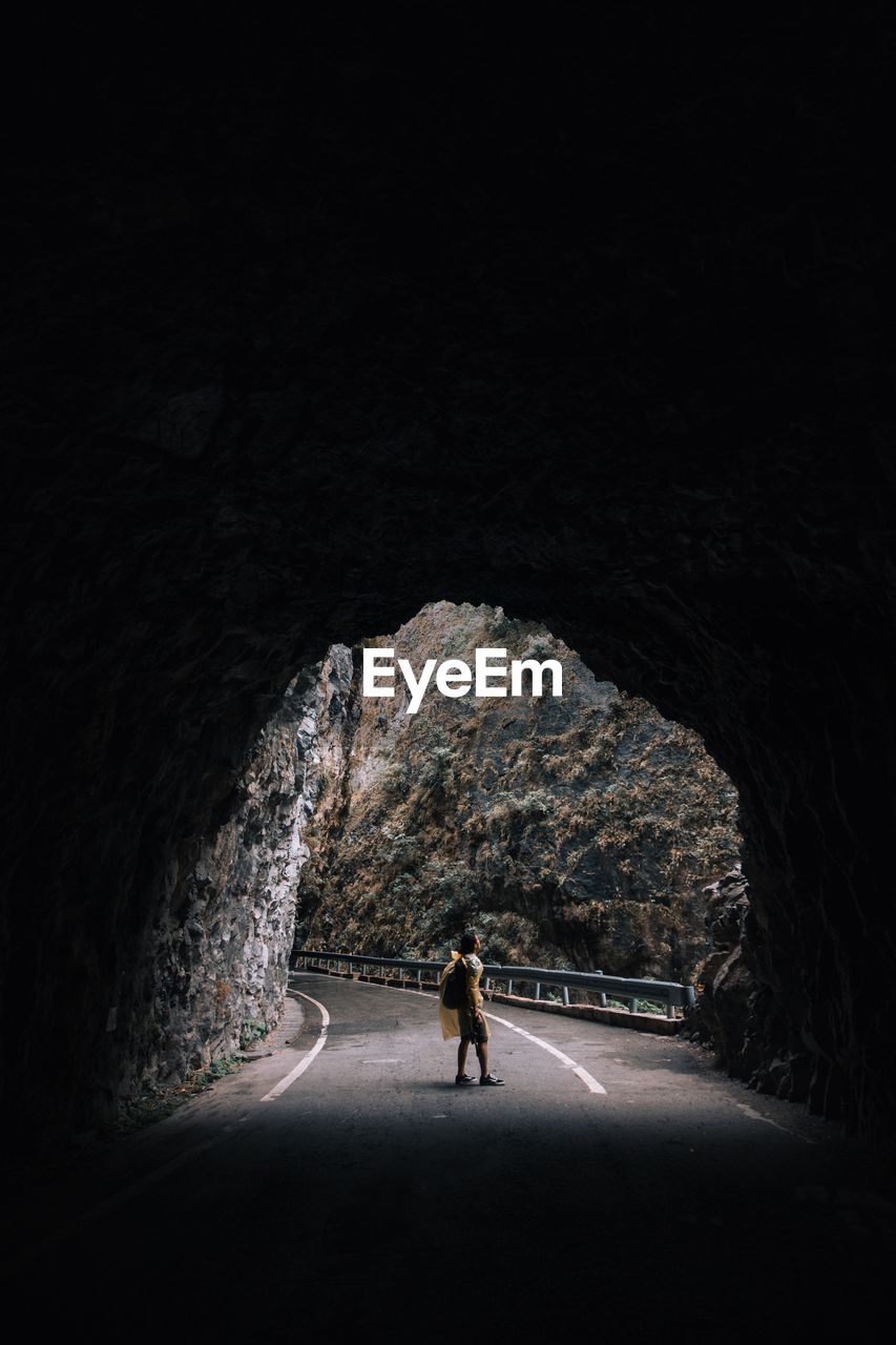 Side view of man standing on road seen through tunnel