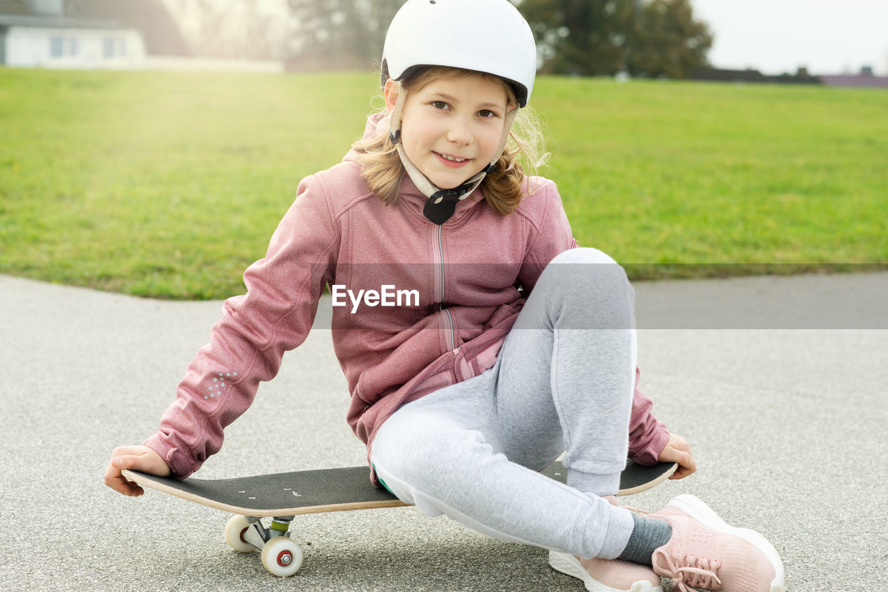 Portrait of smiling girl sitting on skateboard at park