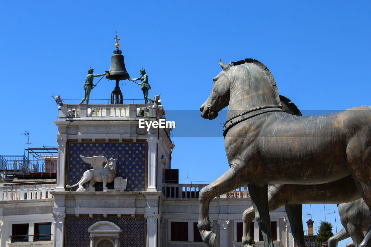 Low angle view of statues and building in city against clear blue sky