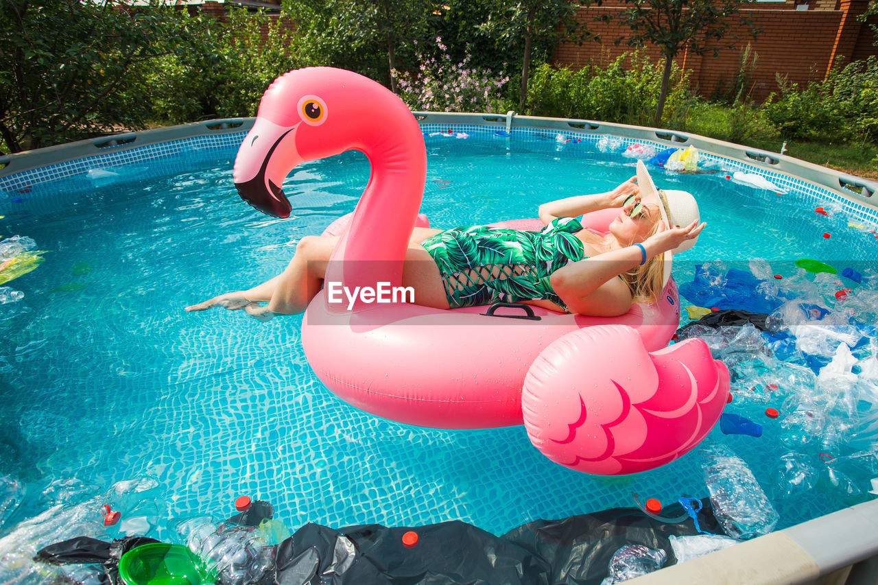 HIGH ANGLE VIEW OF YOUNG WOMAN FLOATING IN SWIMMING POOL