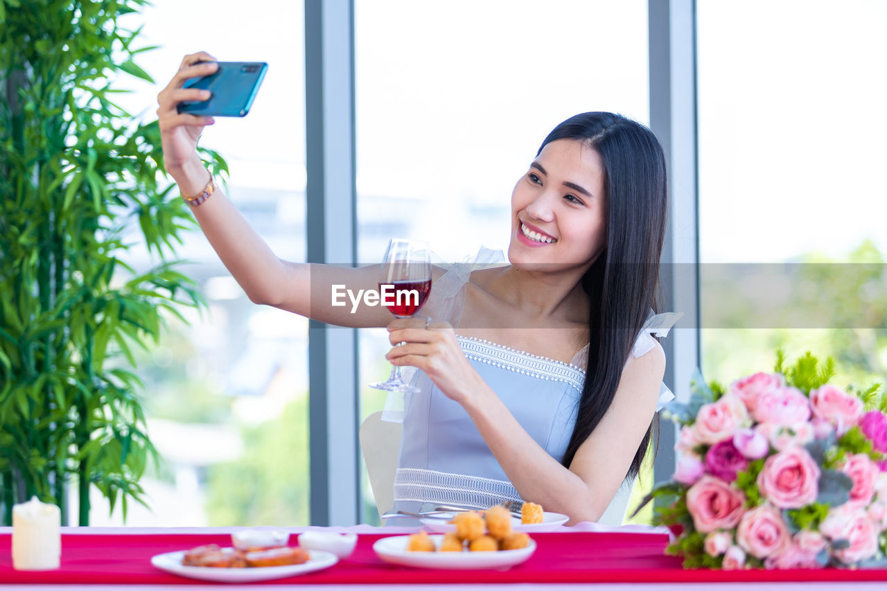 YOUNG WOMAN SMILING WHILE HOLDING DRINK IN GLASS