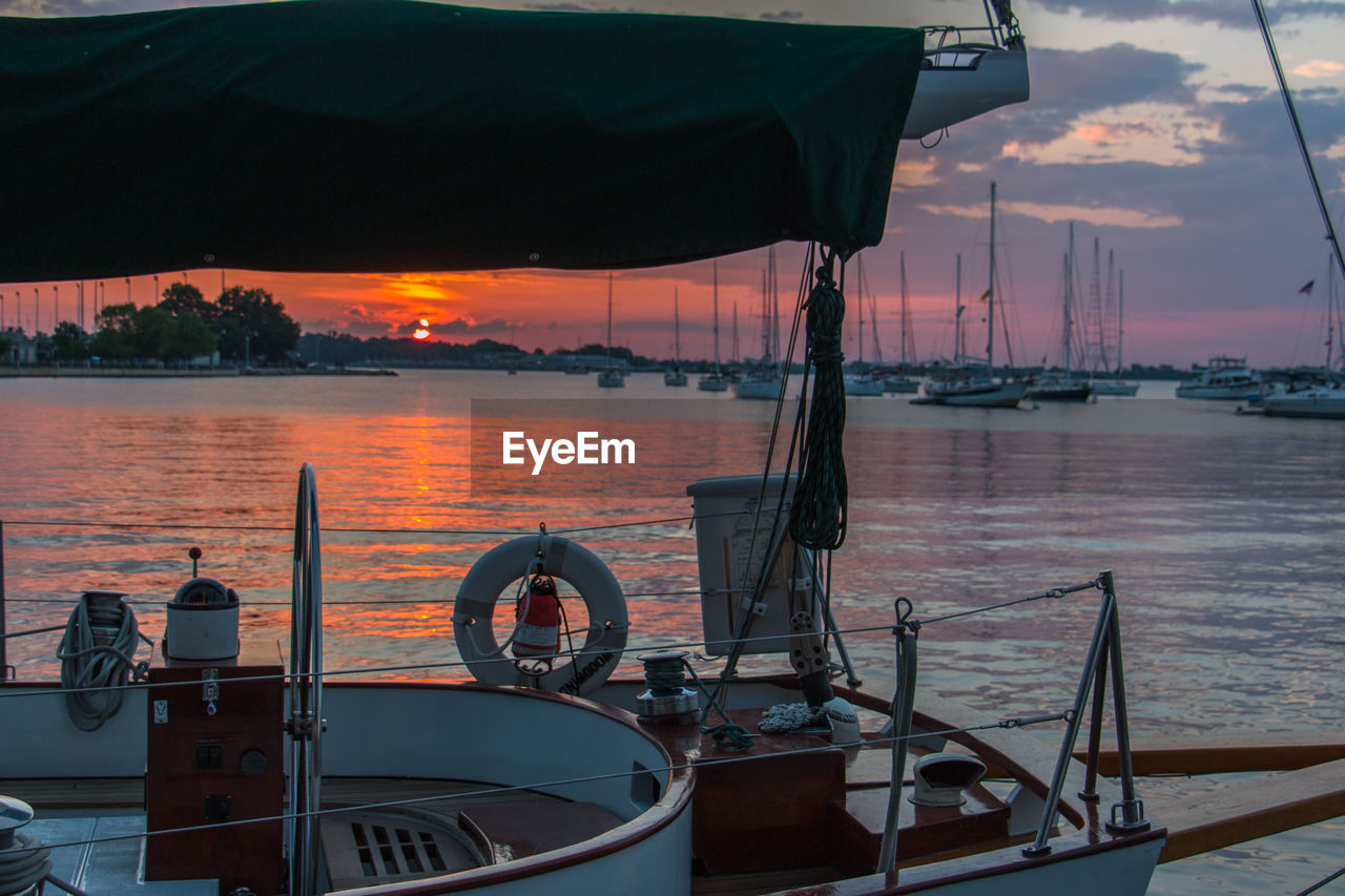 Sailboats moored in harbor at sunset