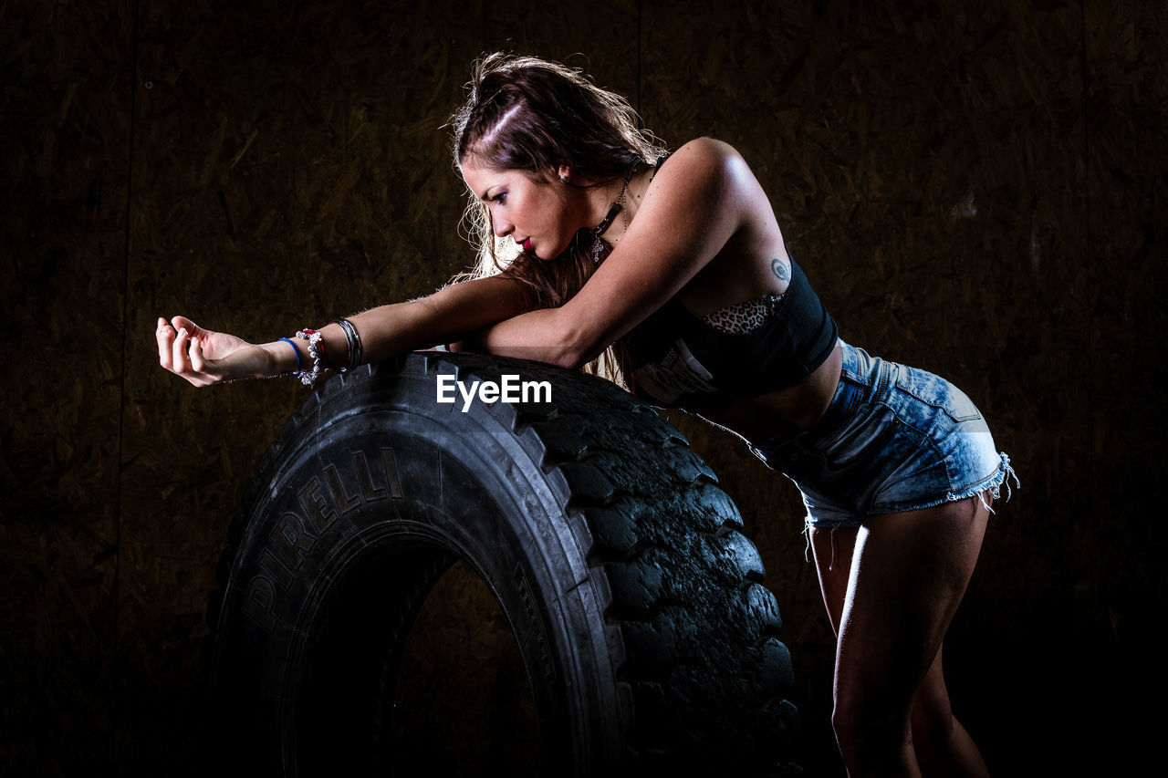 Side view of woman standing by tire at gym