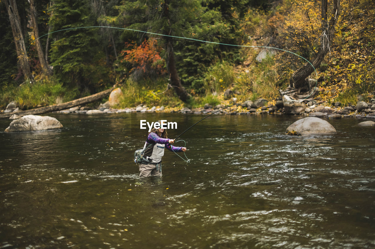 Woman fly fishing at roaring fork river in forest during autumn