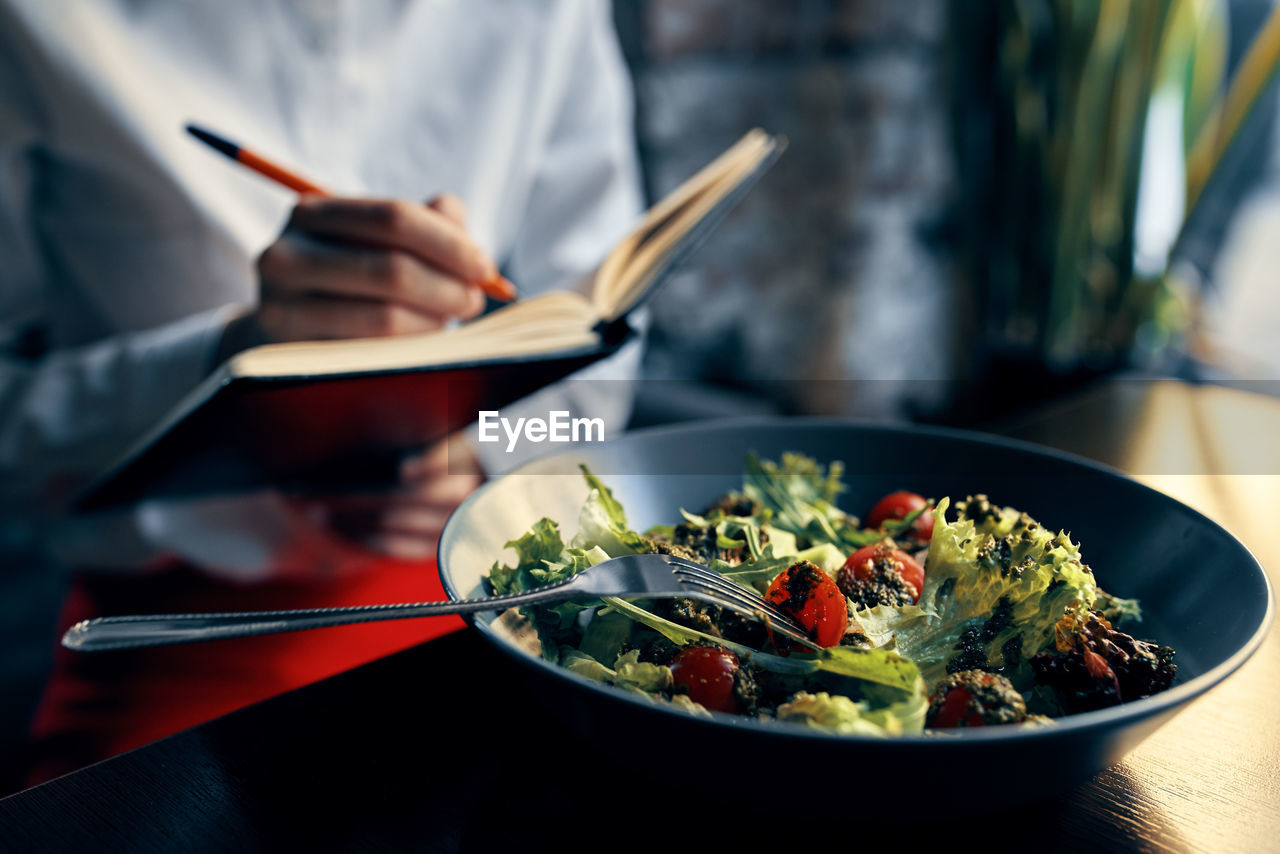 Midsection of chef writing in diary in front of food in plate