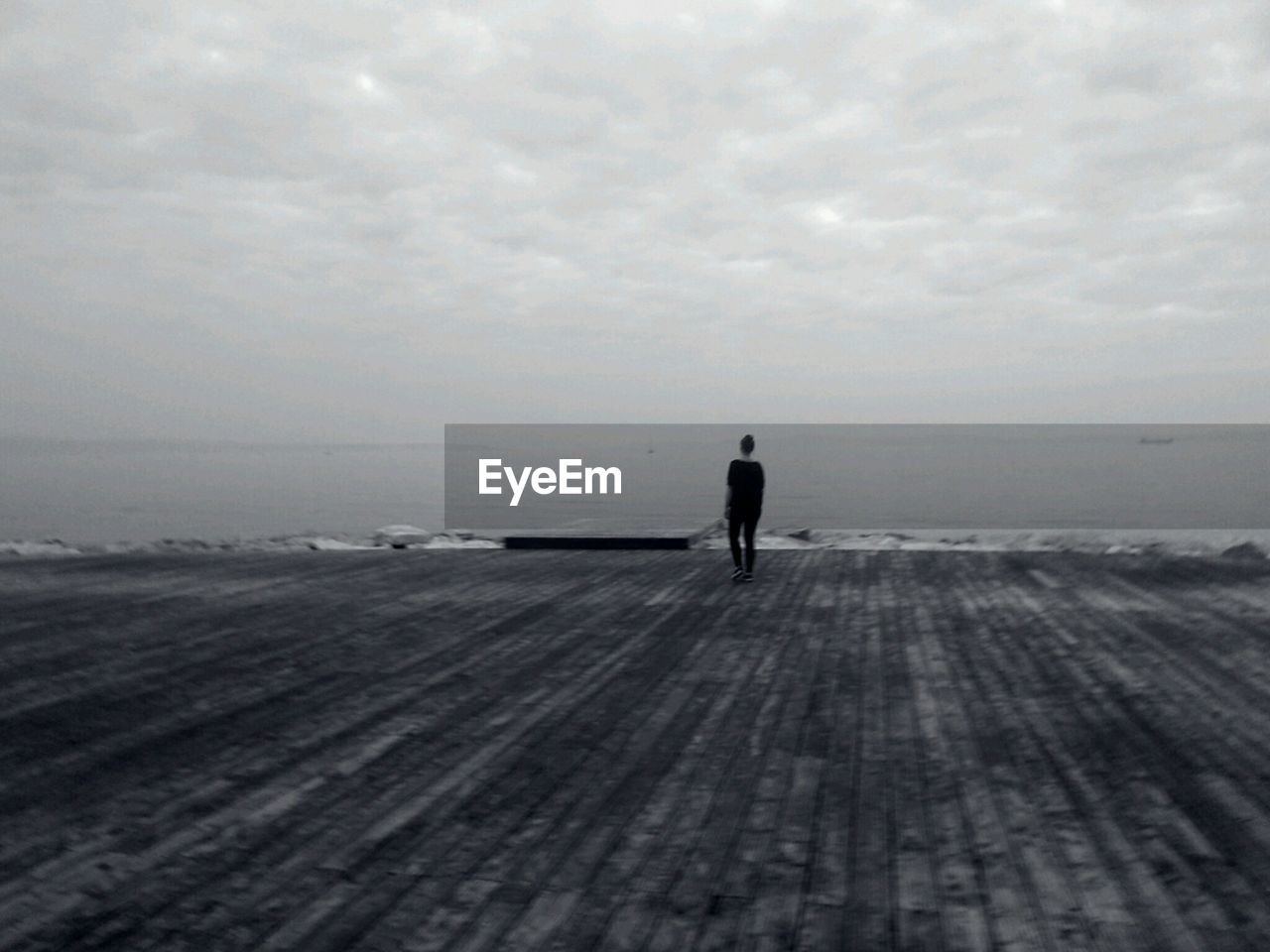 Rear view of woman looking at sea while standing on pier against sky