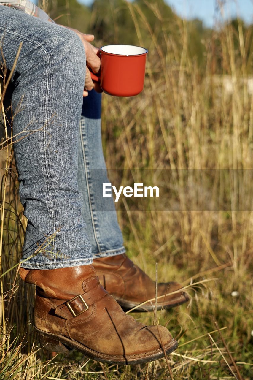 Low section of farmer having coffee while sitting at farm during sunny day