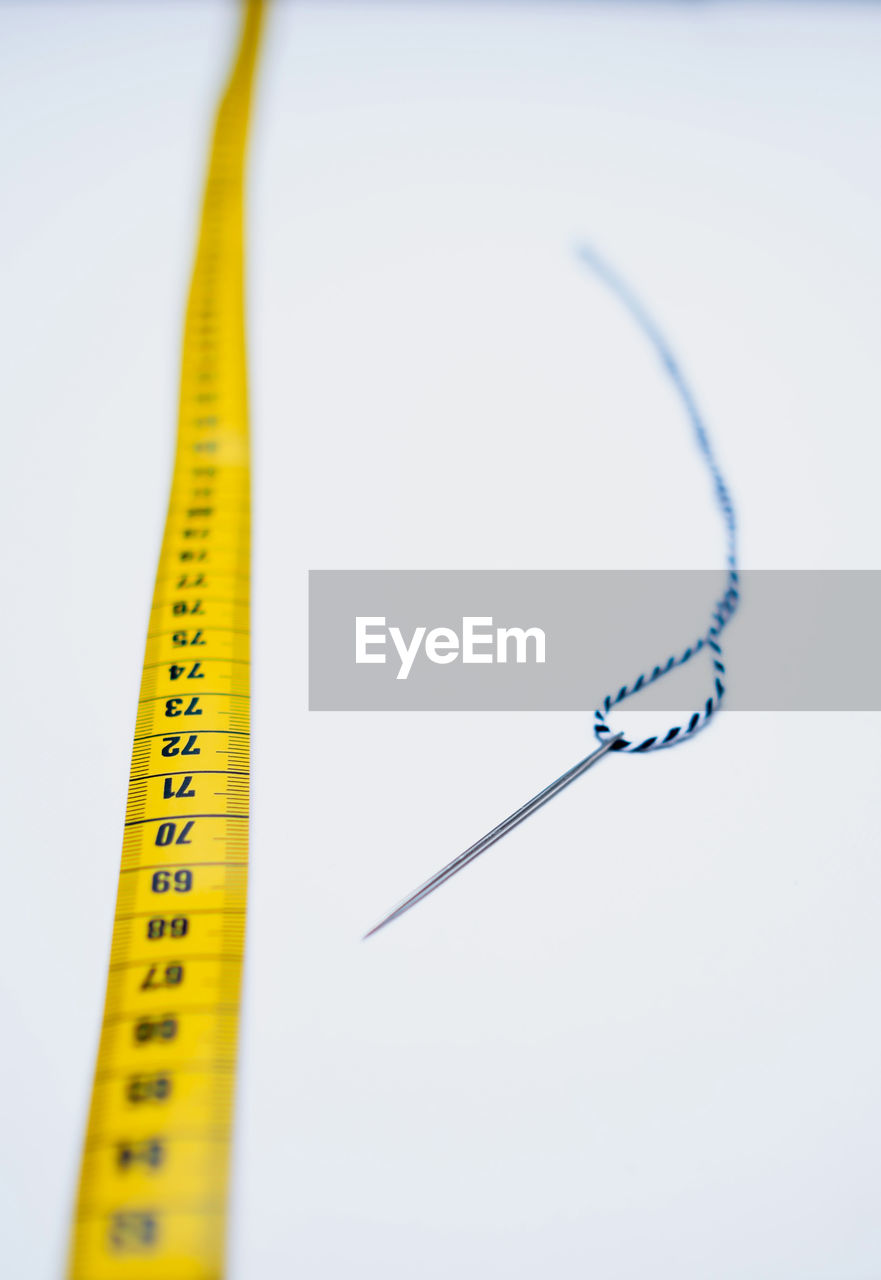 High angle view of tailoring tools like needle, tape measure and yarn against white background.