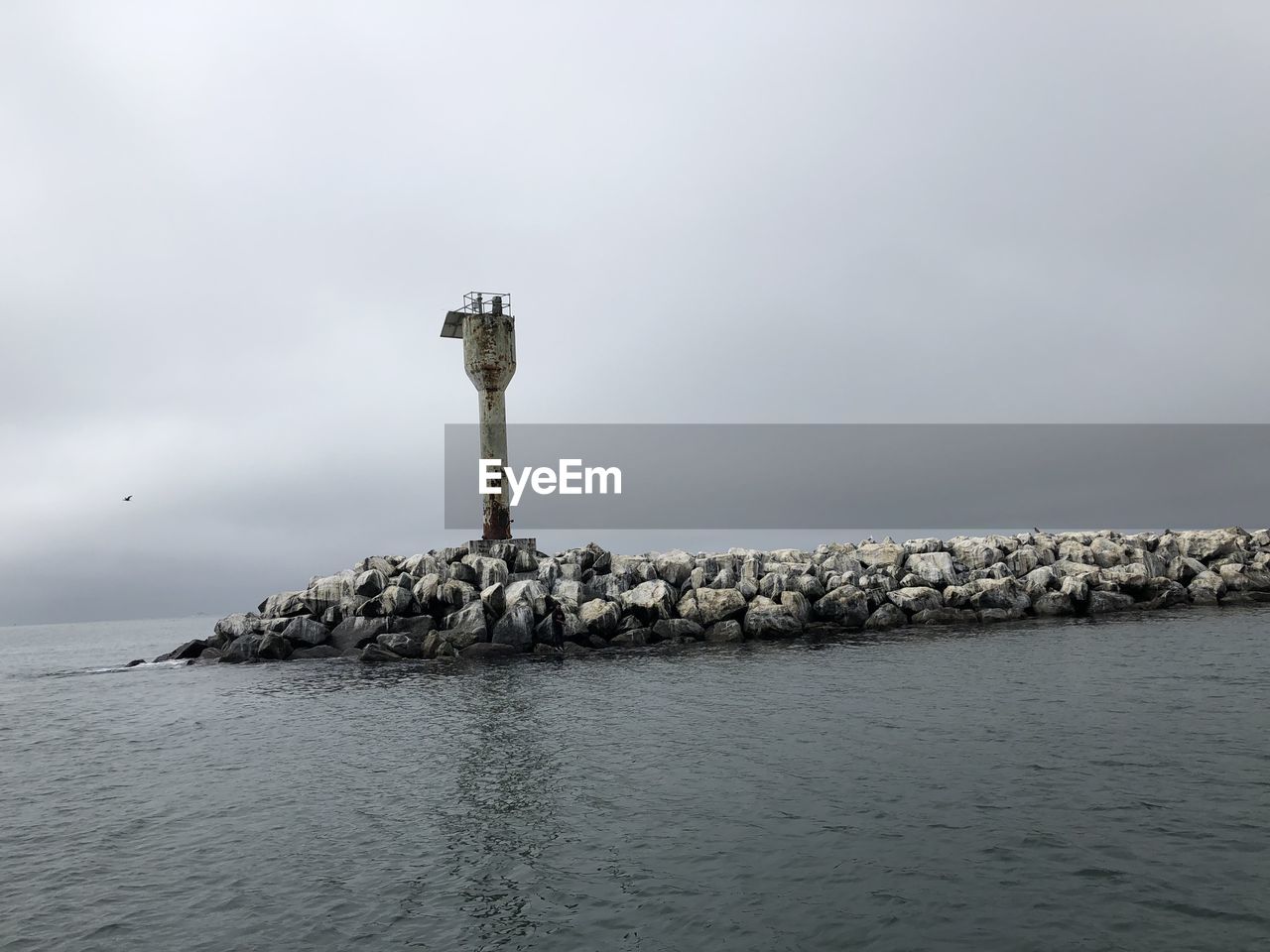 Lighthouse on rock by sea against sky