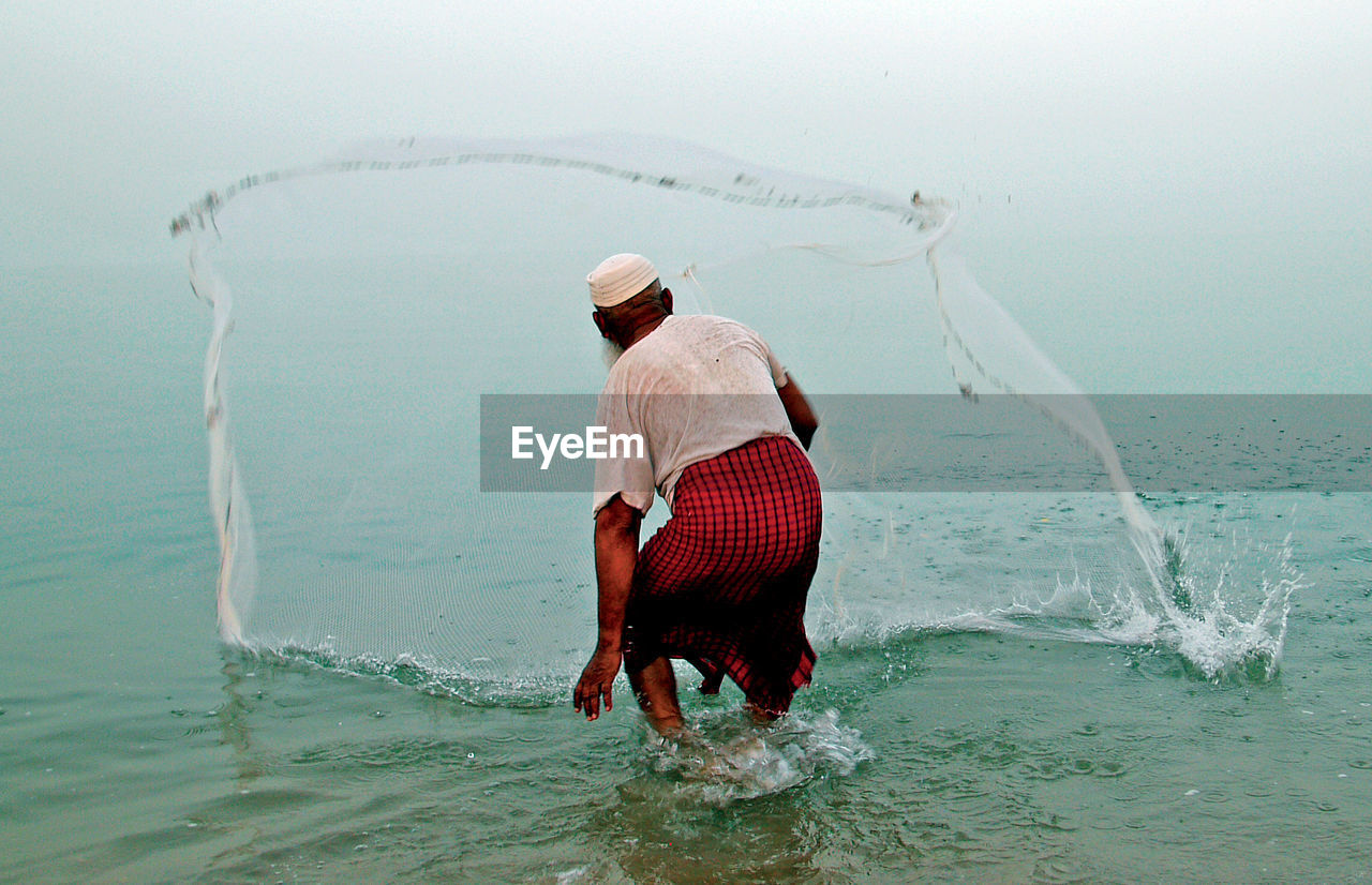 REAR VIEW OF MAN WITH FISHING NET ON SEA