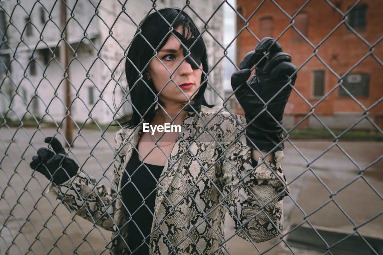 Portrait of young woman seen through chainlink fence