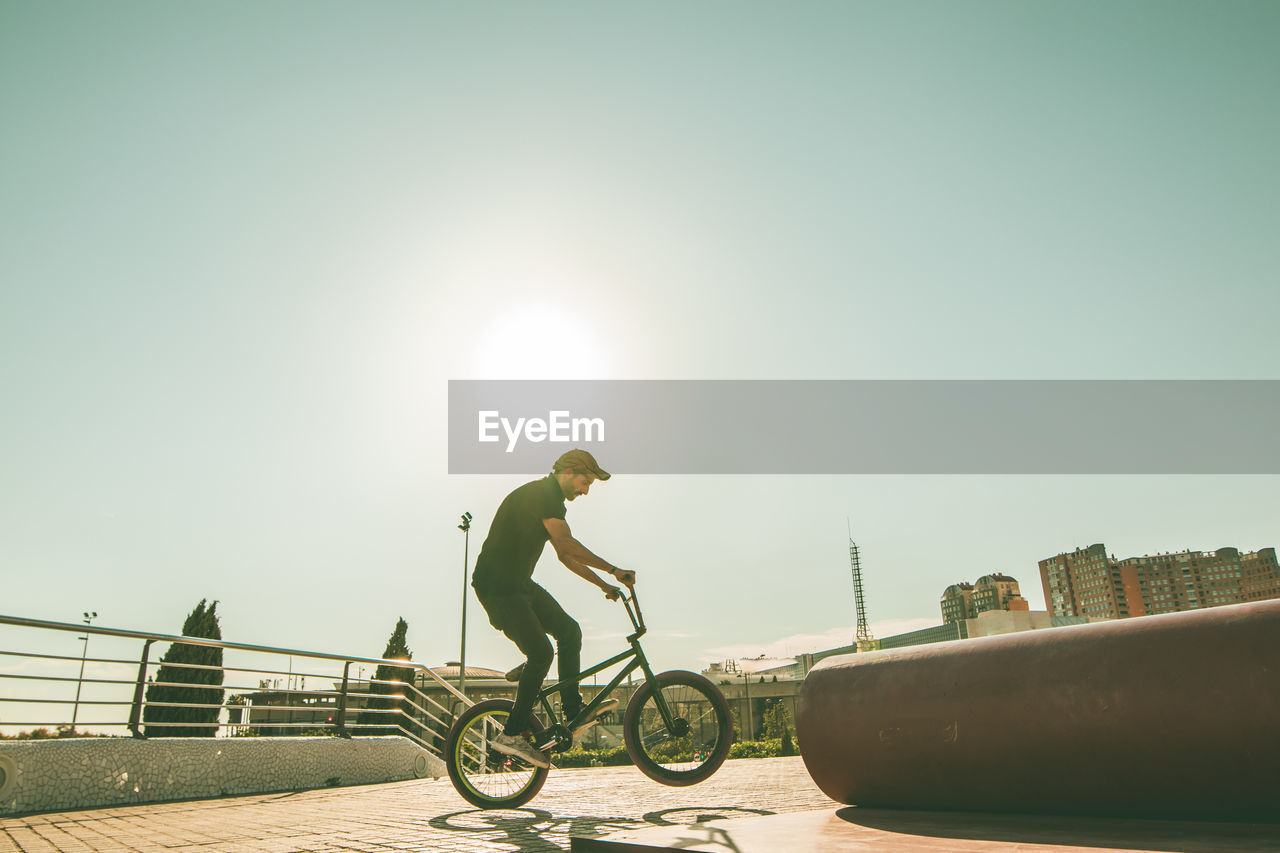 Man riding bicycle on metallic pipe against sky