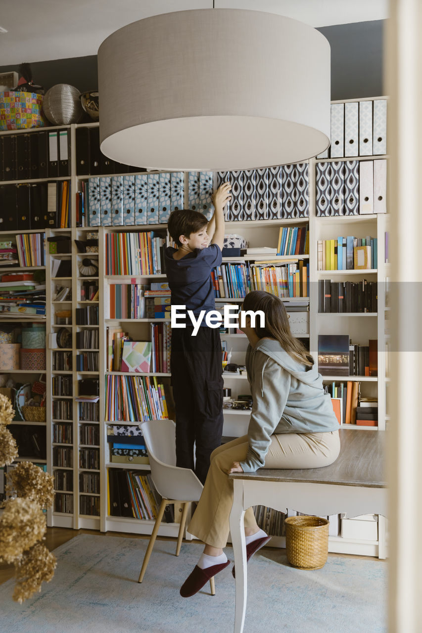 Side view of teenage girl looking at boy removing file from rack at home