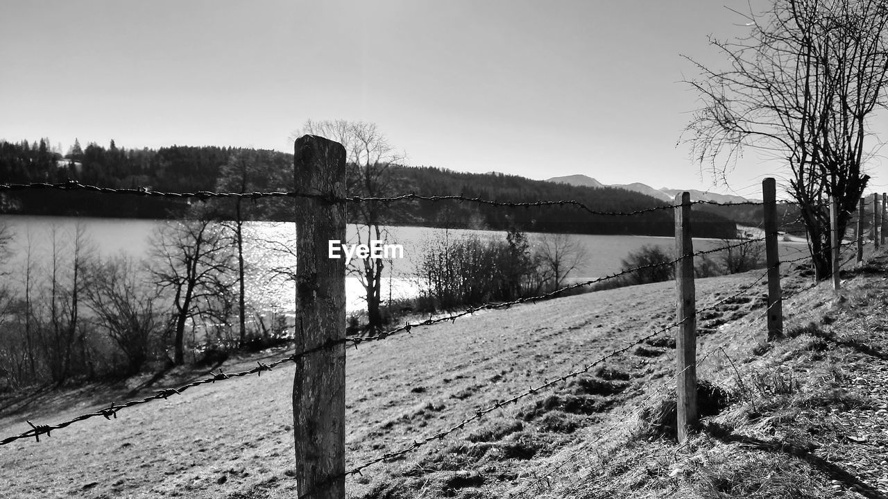 fence, sky, nature, winter, black and white, monochrome, landscape, monochrome photography, plant, tree, land, snow, tranquility, security, rural area, tranquil scene, no people, environment, split-rail fence, protection, scenics - nature, water, non-urban scene, beauty in nature, day, wood, rural scene, field, outdoors, mountain, gate, barbed wire, morning, wire, black, remote, clear sky