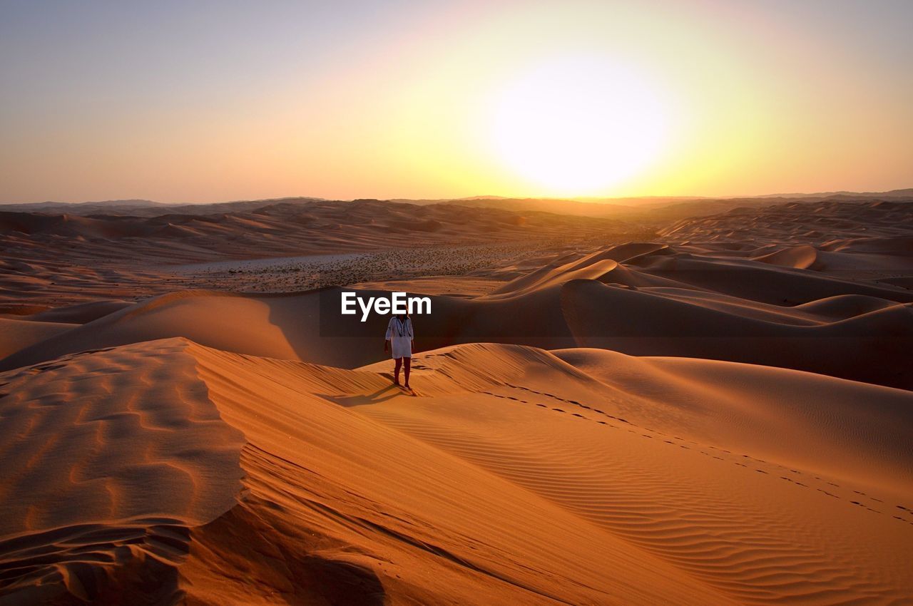 Woman walking on desert against sky during sunset