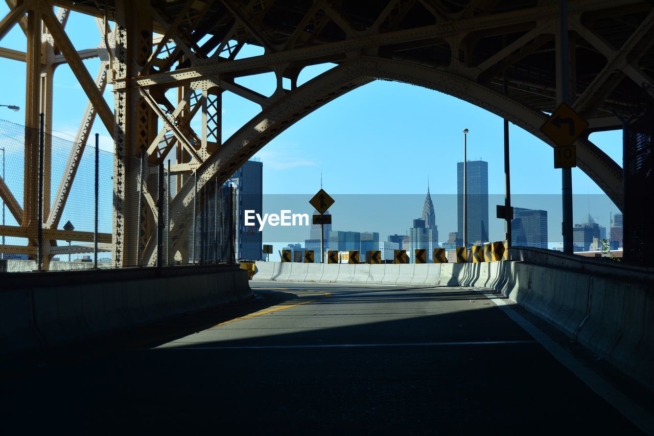 Empty queensboro bridge by modern buildings against clear blue sky