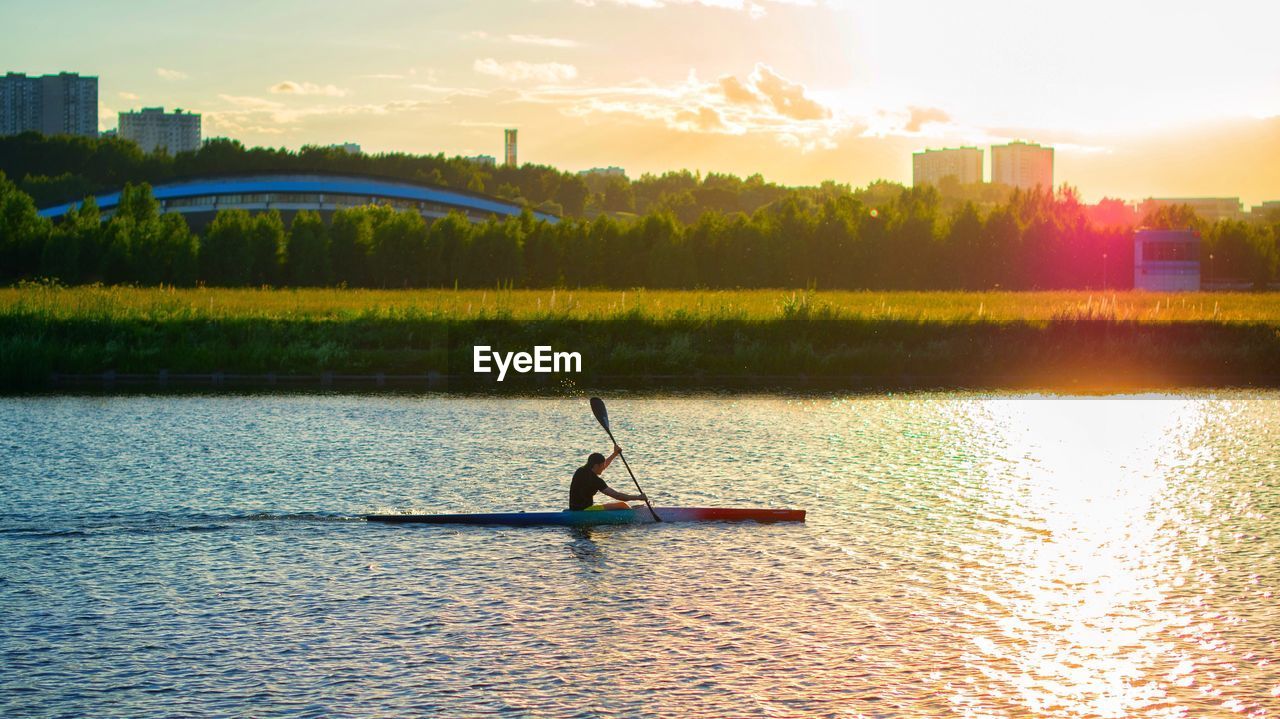 Man rowing on river against sky at sunset