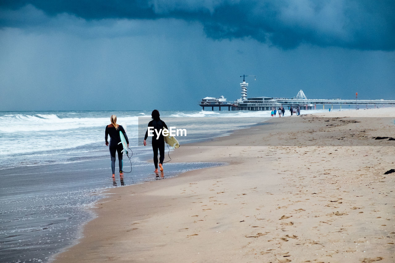 Rear view of surfers walking on shore at beach
