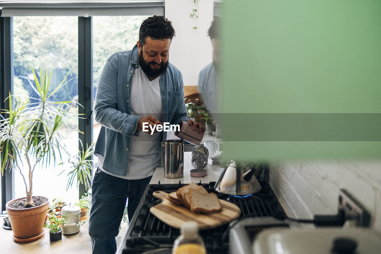 Man preparing coffee while standing at kitchen counter