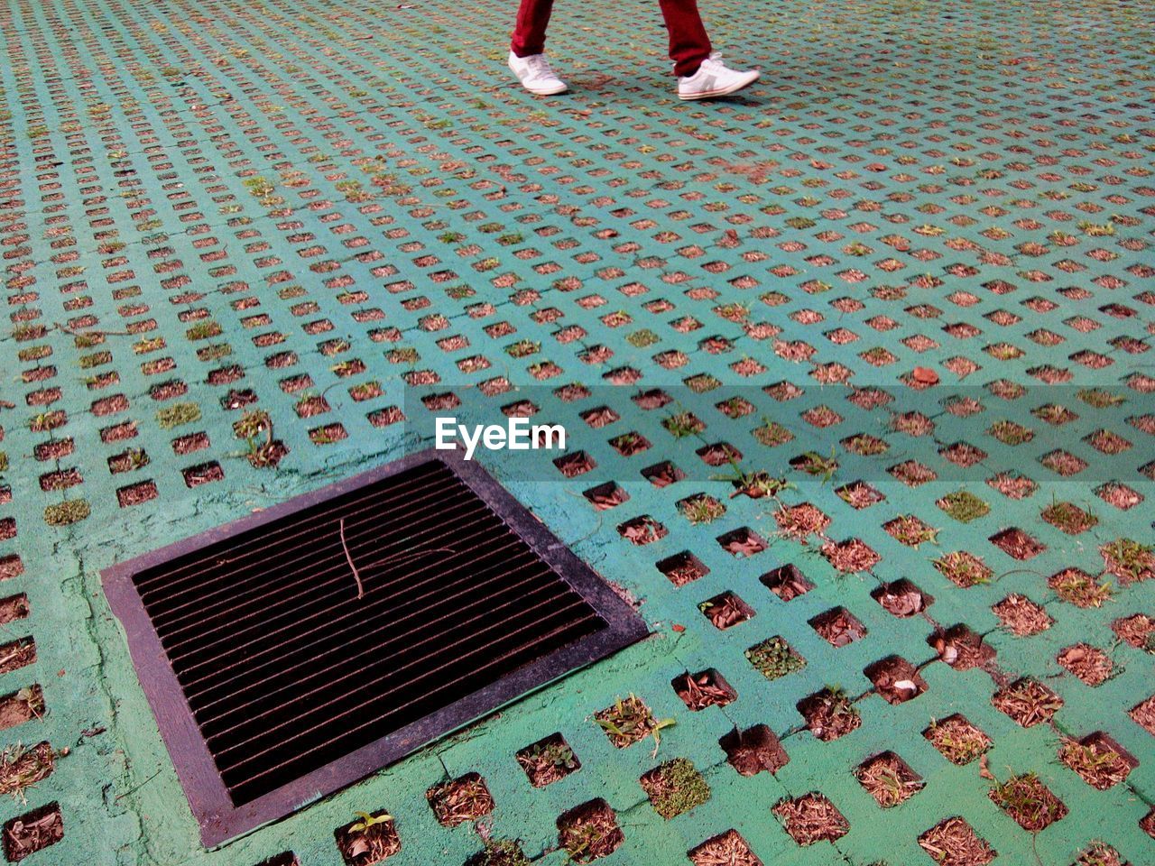 Close-up of metal grate manhole lid amidst concrete hole walkway