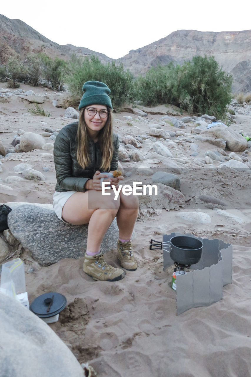 Portrait of hiker holding coffee cup while sitting on rock