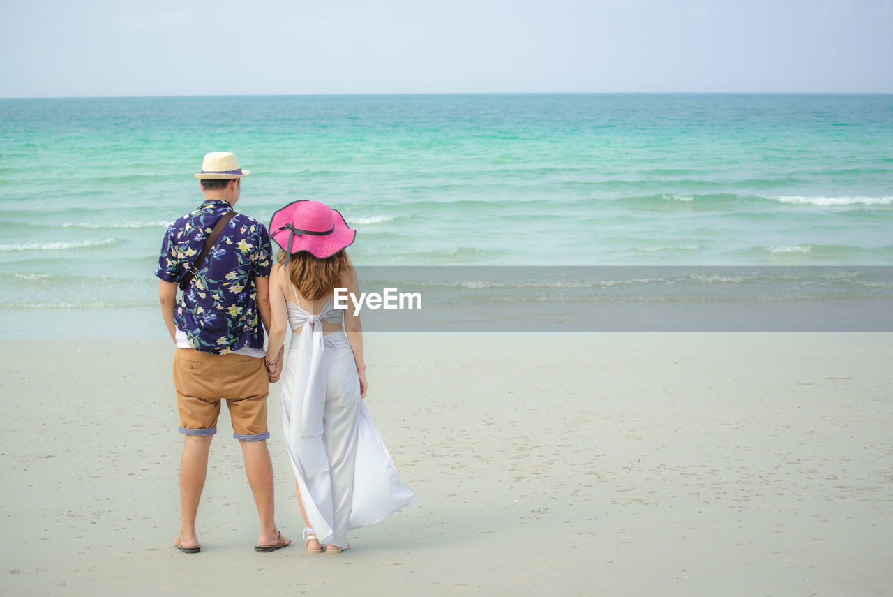 Rear view of couple holding hands while standing at beach