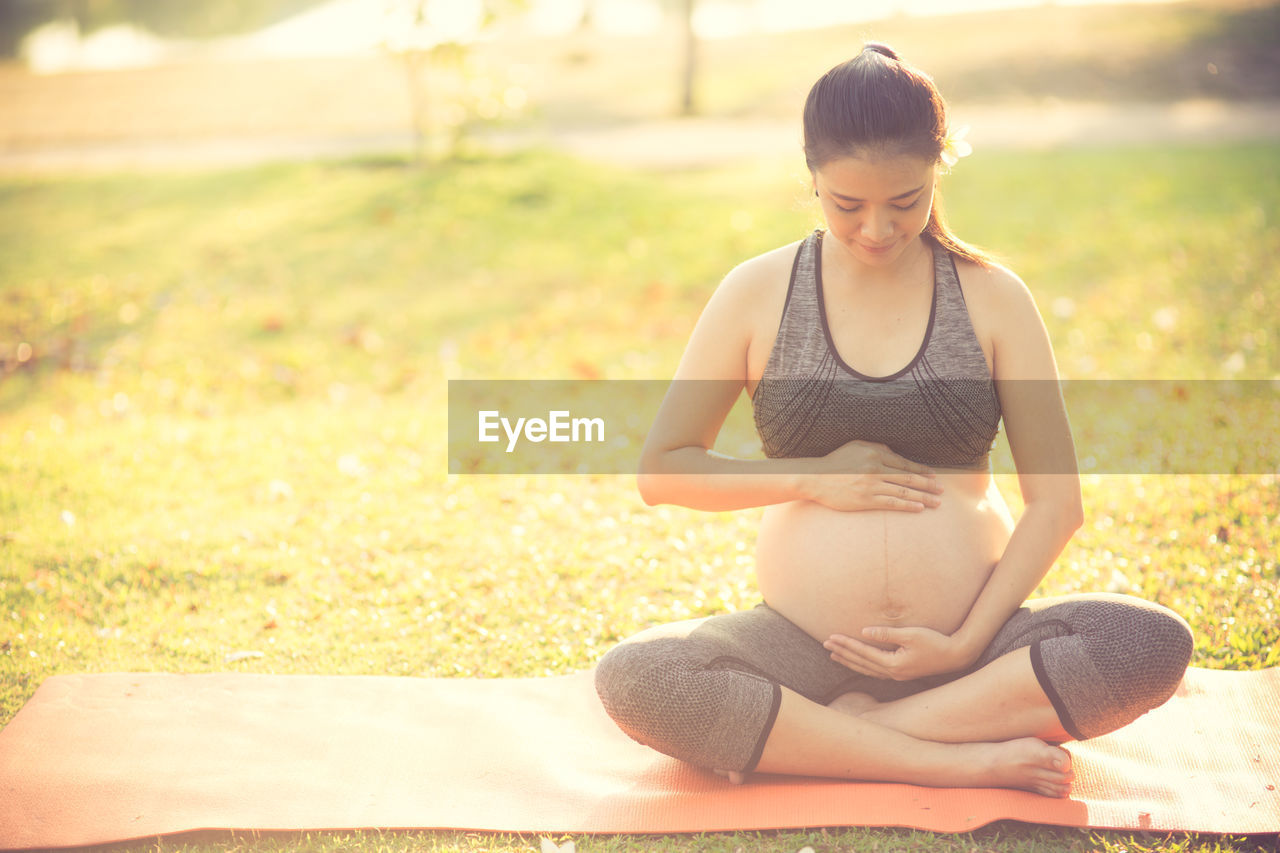 Pregnant woman touching belly while sitting on field