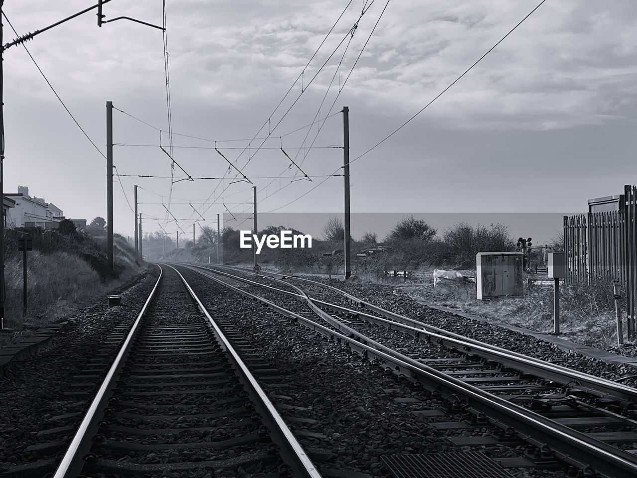 railroad track, track, rail transportation, transportation, cable, sky, electricity, transport, railway, line, black and white, power line, electricity pylon, cloud, mode of transportation, power supply, technology, monochrome, nature, no people, vehicle, public transportation, vanishing point, the way forward, architecture, monochrome photography, travel, residential area, lane, train station, diminishing perspective, power generation, outdoors, day, railroad station, train, built structure, city, overhead power line, parallel