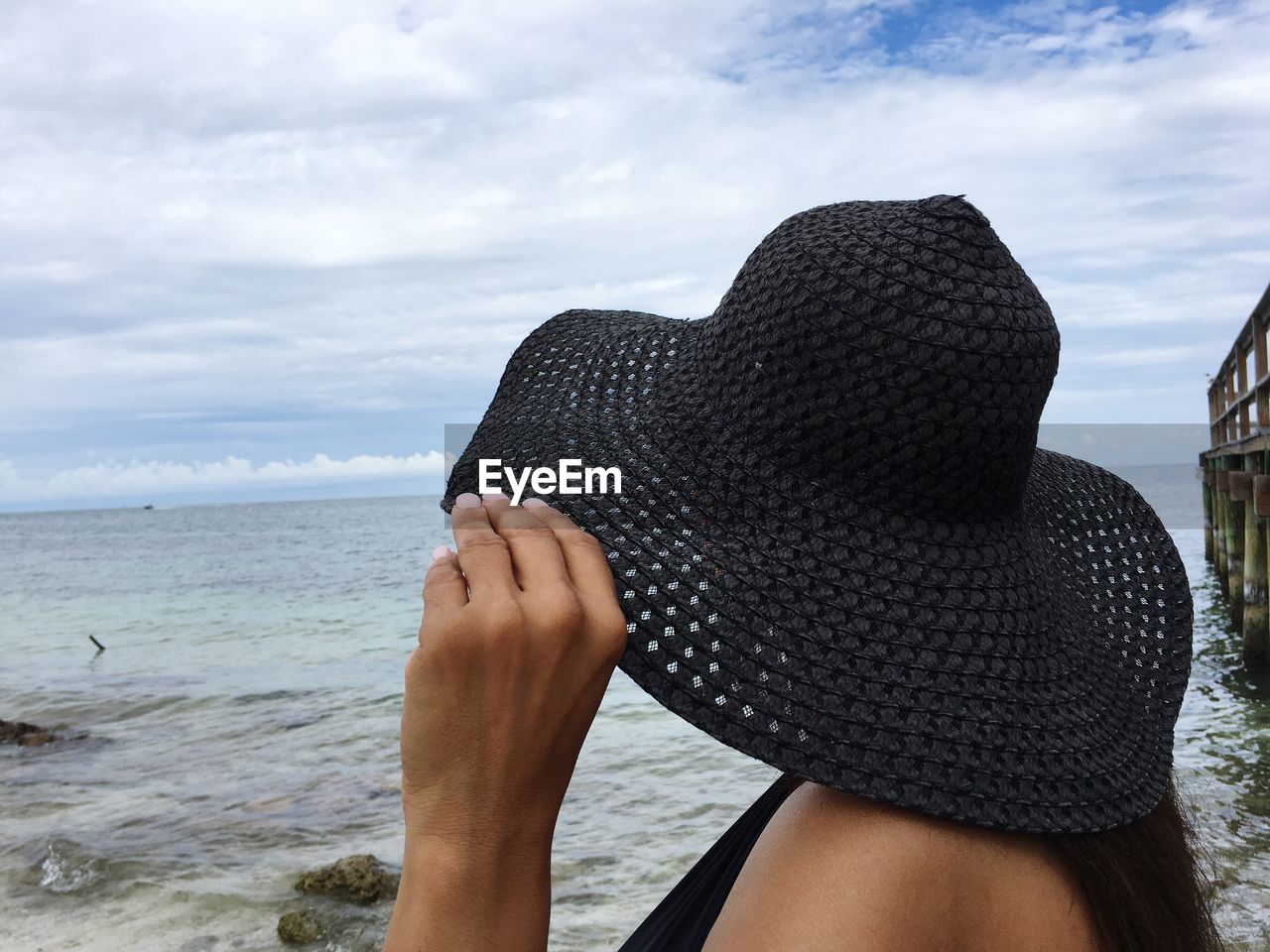 Close-up of woman wearing sun hat while standing at beach against sky