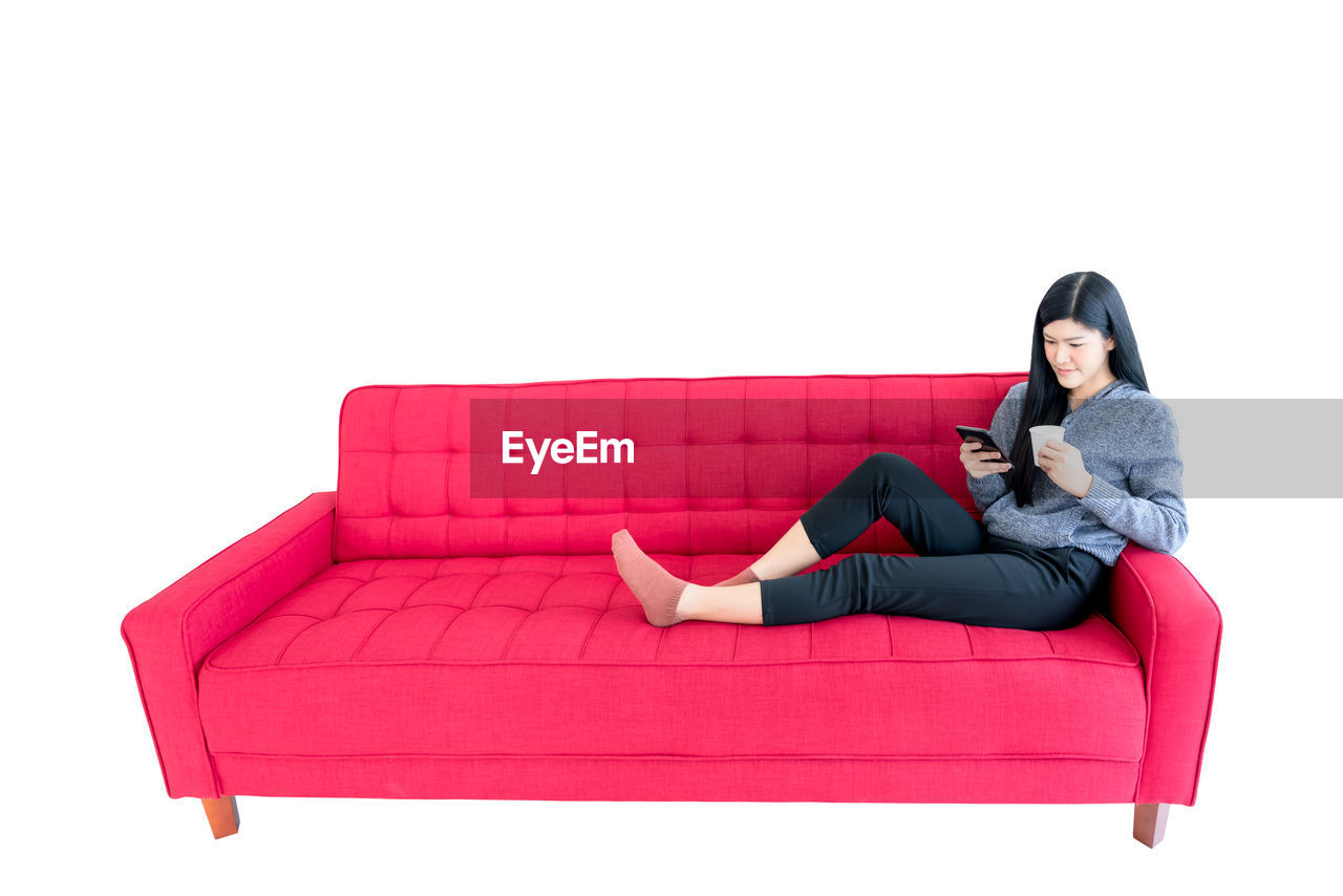 WOMAN SITTING ON SOFA AGAINST GRAY BACKGROUND