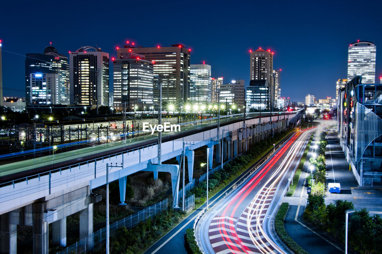 Light trails on road amidst buildings against sky at night