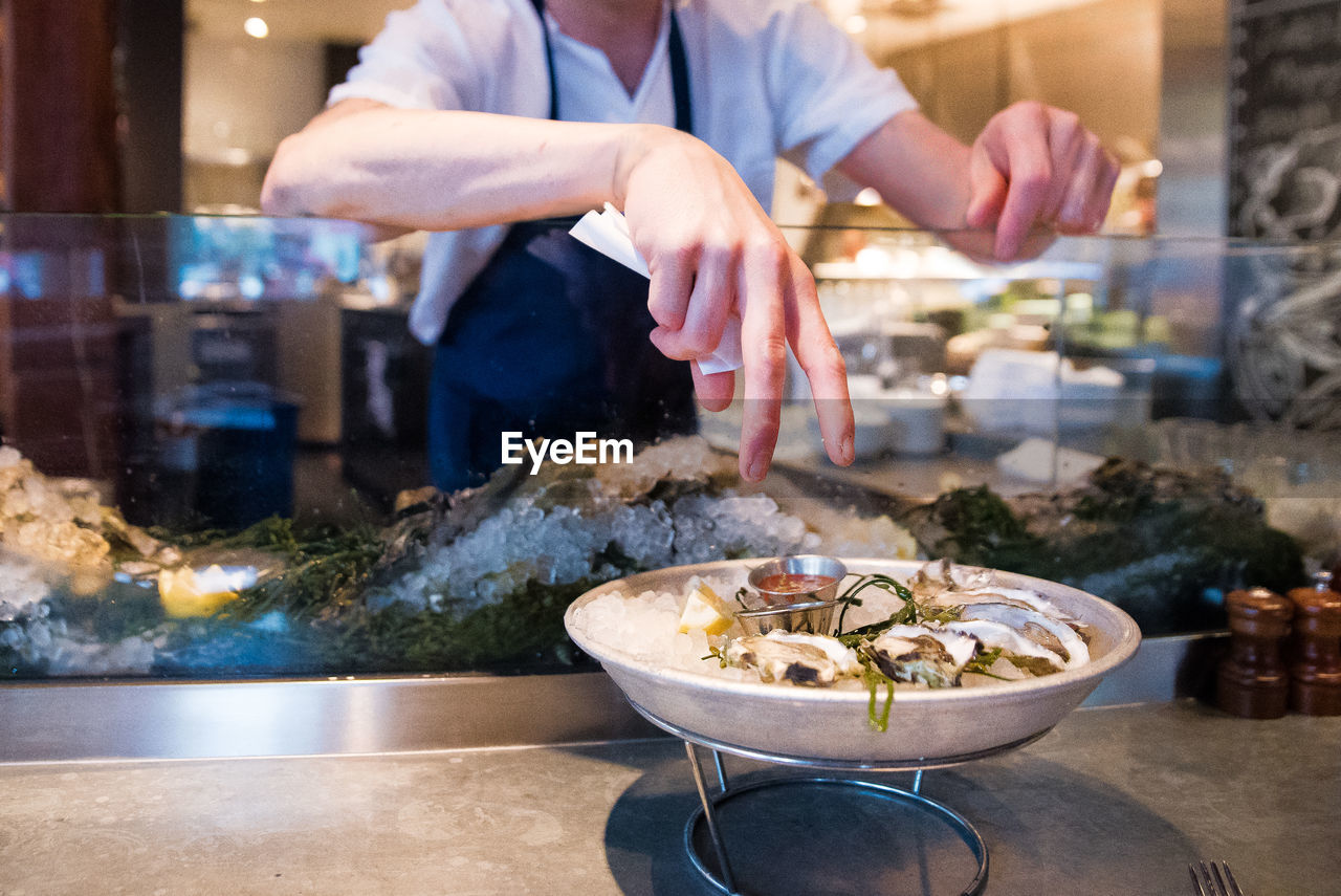 Midsection of man hand over oysters on table at restaurant