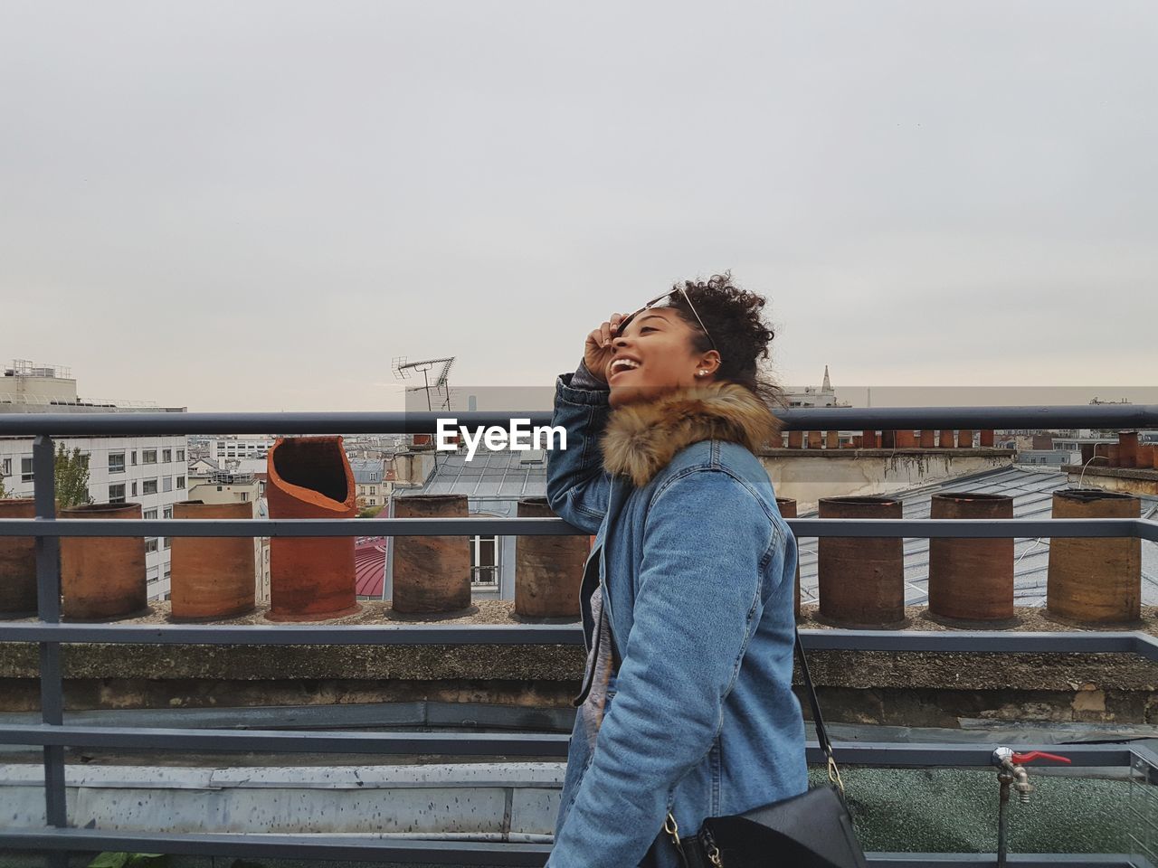 Smiling woman standing by railing on bridge against sky