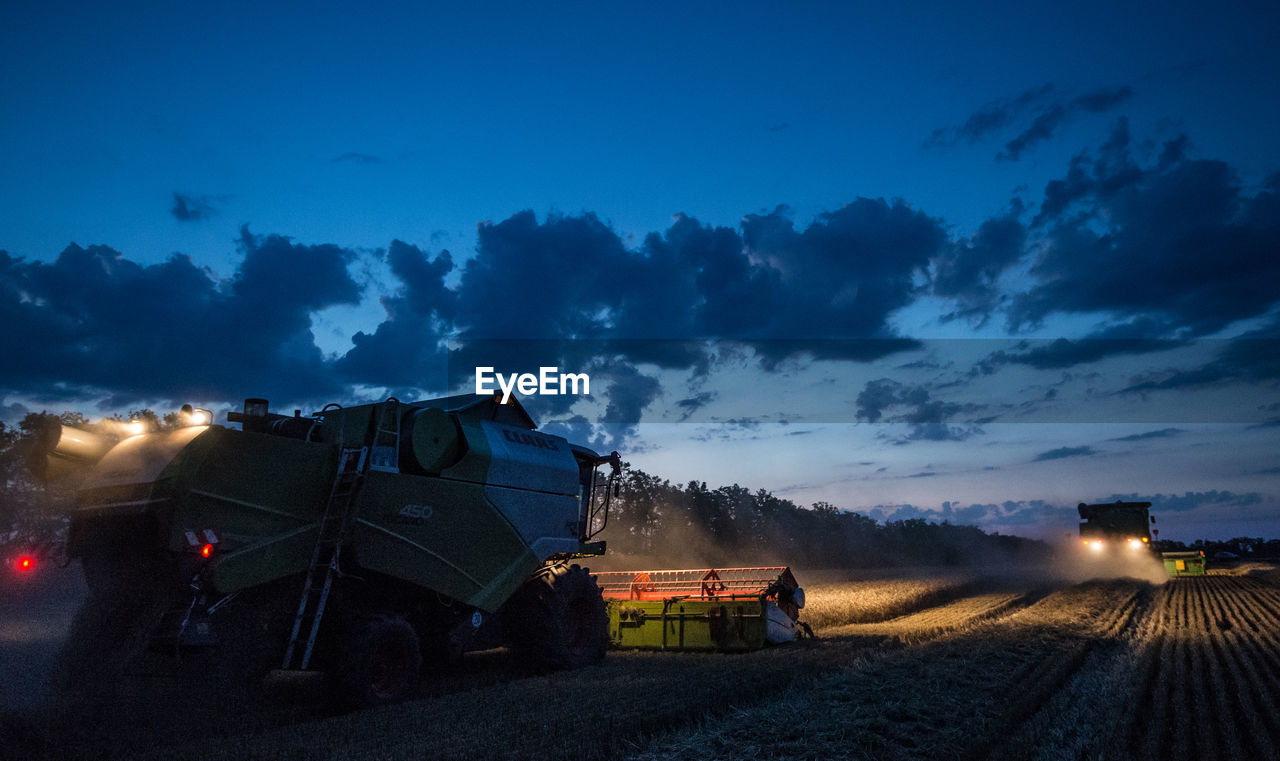 Low angle view of combine harvesters against sky during dusk