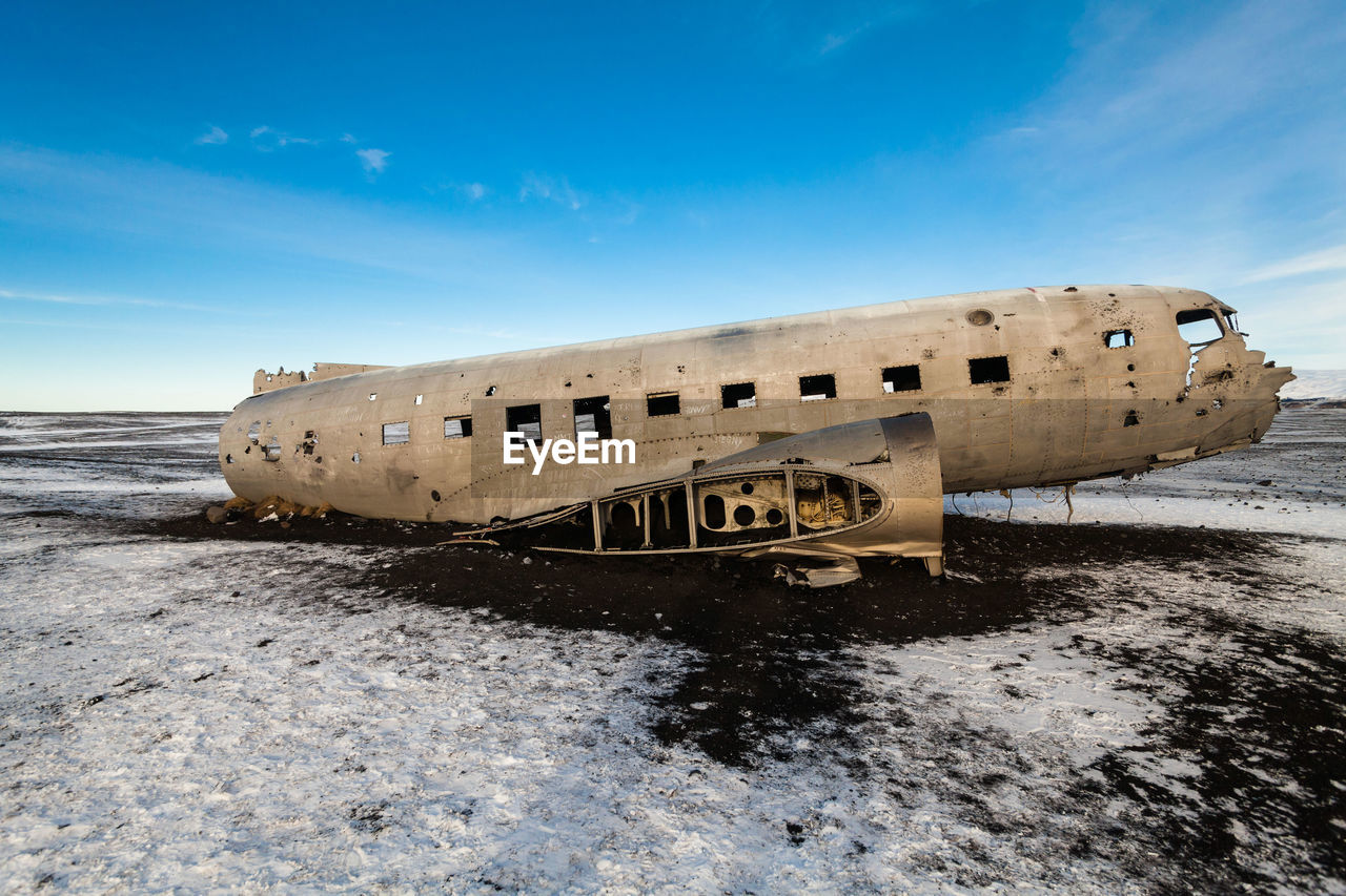 Abandoned airplane crash on snowy field against sky during sunset